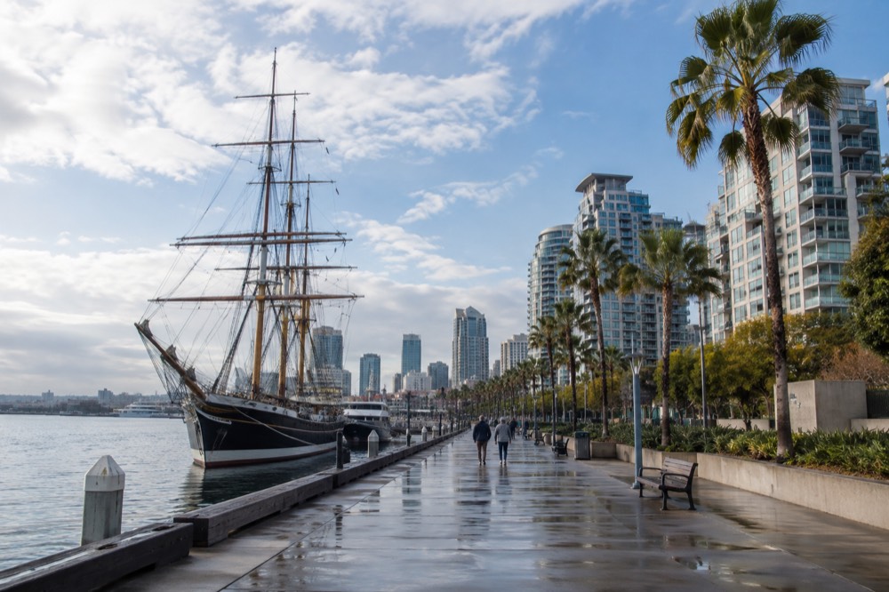 Waterfront promenade with a historic sailing ship, modern condos and palm trees along the bay
