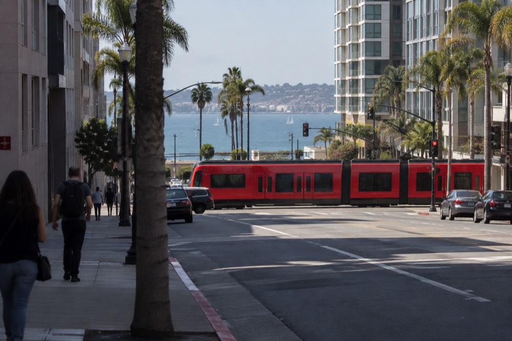 A red trolley crossing a downtown San Diego street with the bay beyond