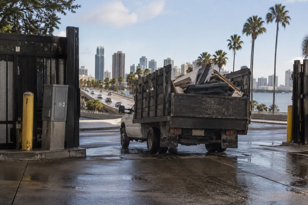 A loaded pickup truck leaving a waste facility gate onto a coastal highway