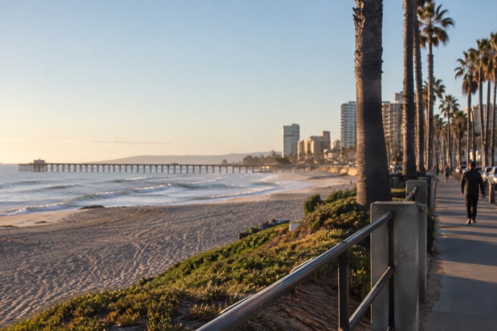 Wide sandy beach with a long wooden pier under a clear sky