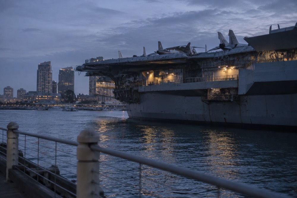 Aircraft carrier flight deck with bay water and city buildings behind it