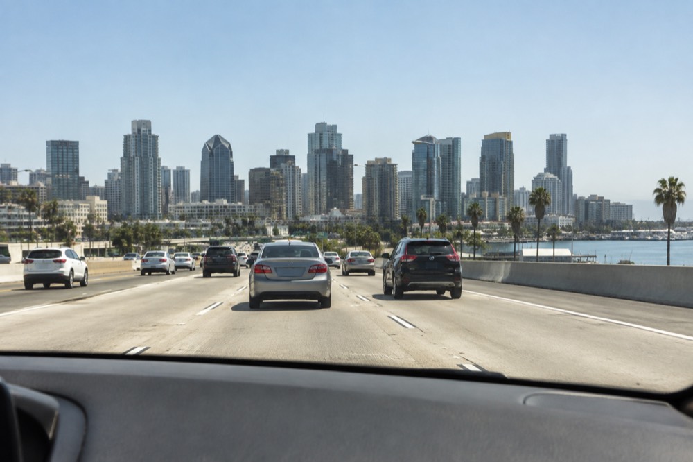 A car driving along a San Diego freeway with the city skyline ahead under a clear sky