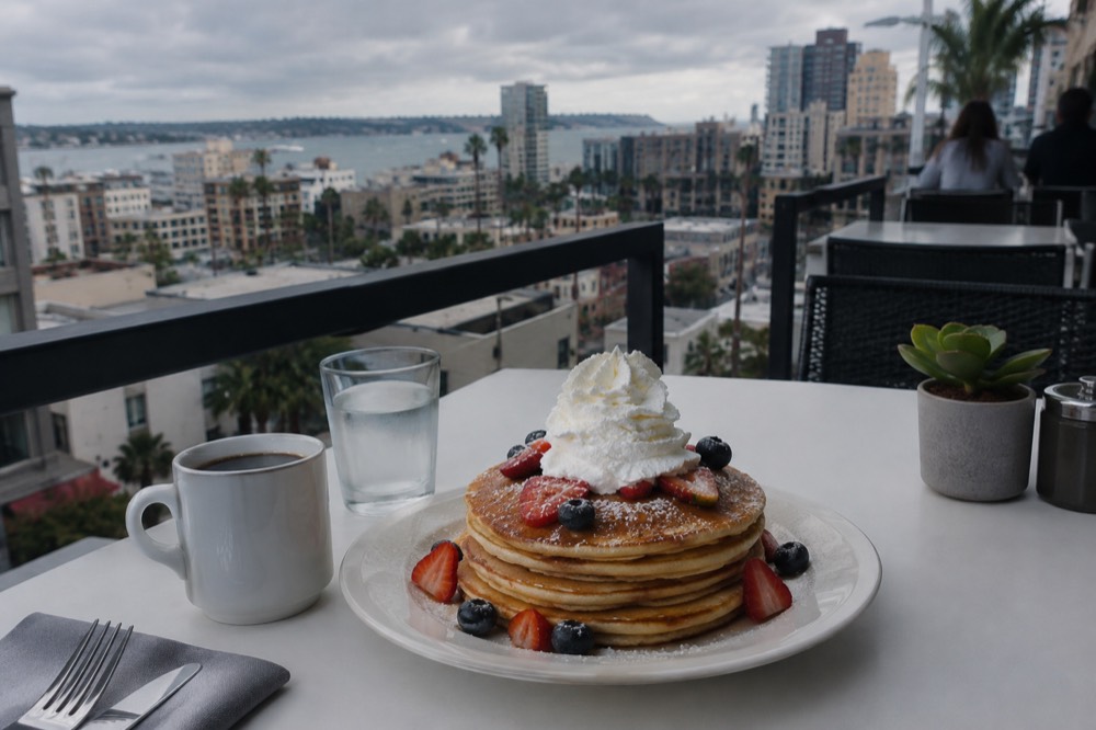A plate of tall stacked pancakes with whipped cream on a bright restaurant table