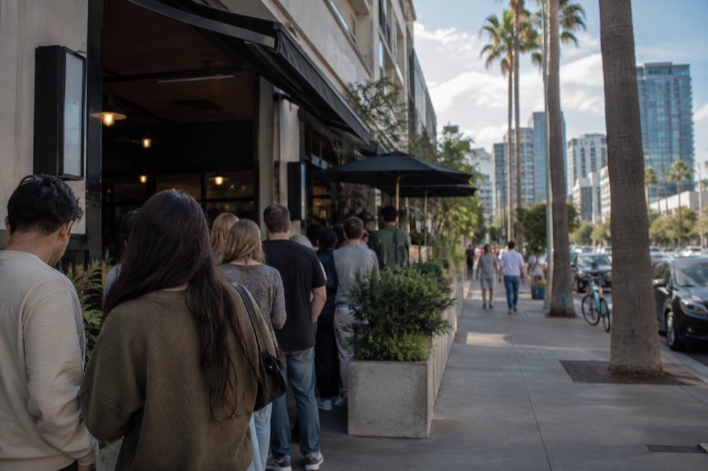 A crowded sidewalk outside a small brunch restaurant with people waiting in line