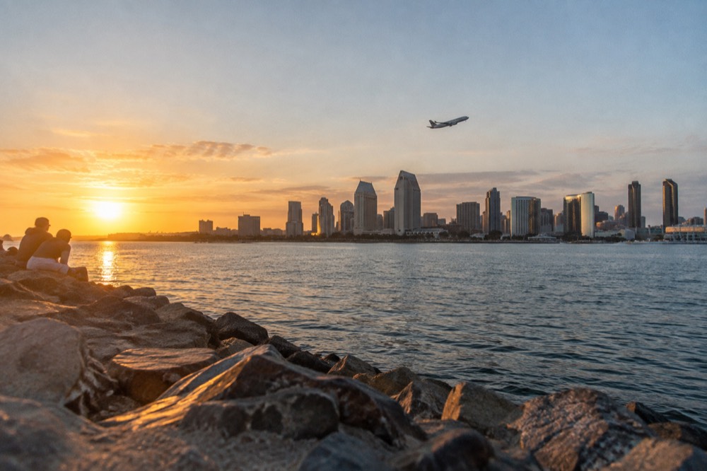 The San Diego skyline across the bay with a plane climbing above the buildings