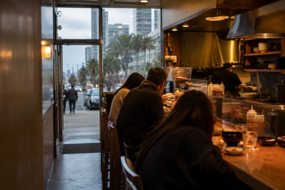 A narrow restaurant interior with a small counter and bar stools in warm light