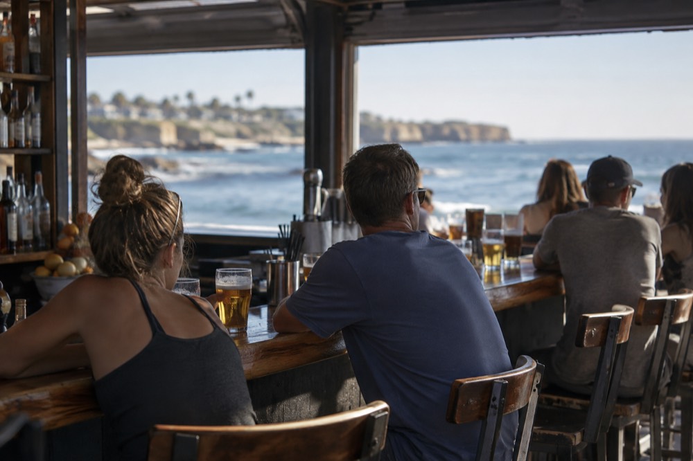 Patrons sitting at a wooden bar with glasses of beer in a neighborhood tavern