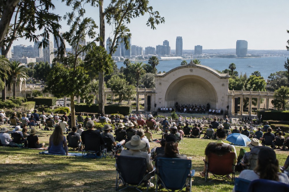 Open-air concert crowd seated on a lawn in front of a park bandshell