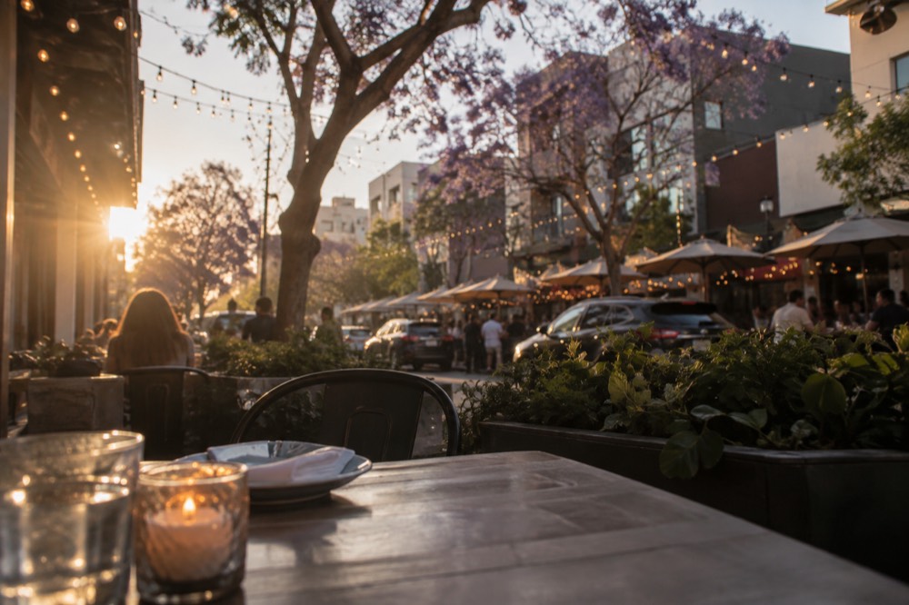 A busy Little Italy street lined with restaurant tables and string lights