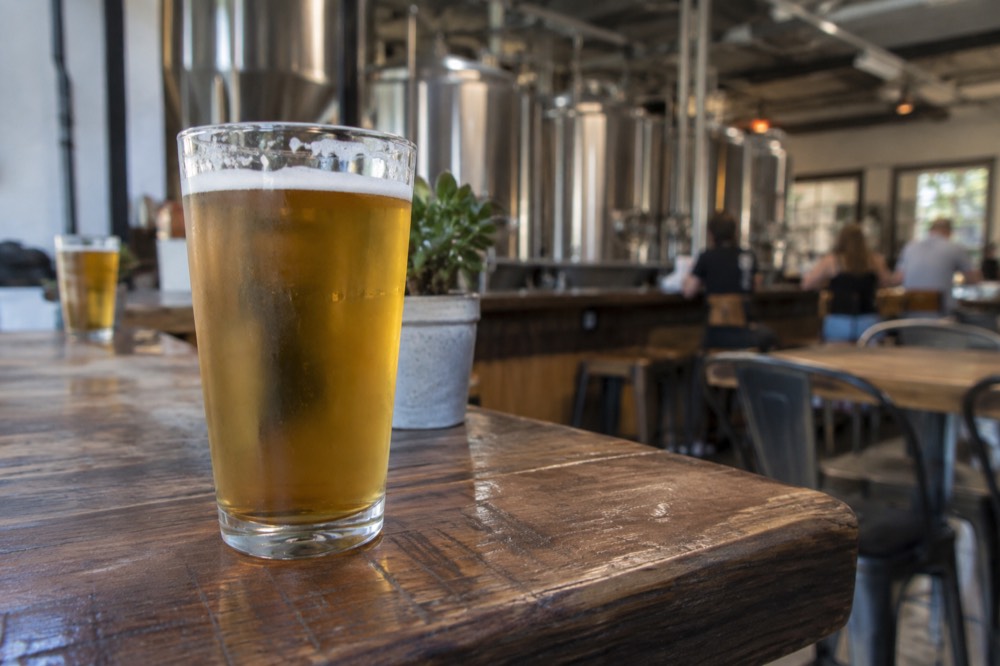 A brewery taproom interior with stainless steel fermentation tanks behind the bar