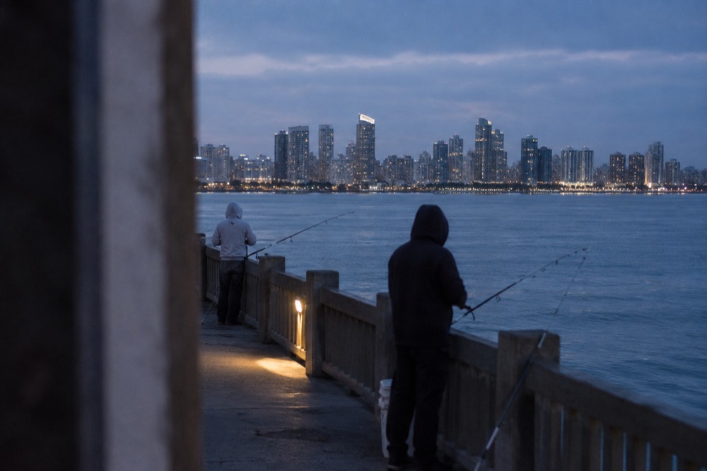 Anglers standing along a concrete pier railing with rods over calm ocean water
