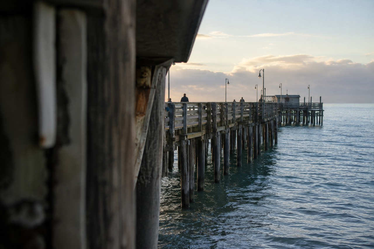 A wooden fishing pier stretching over calm Pacific water in early morning light
