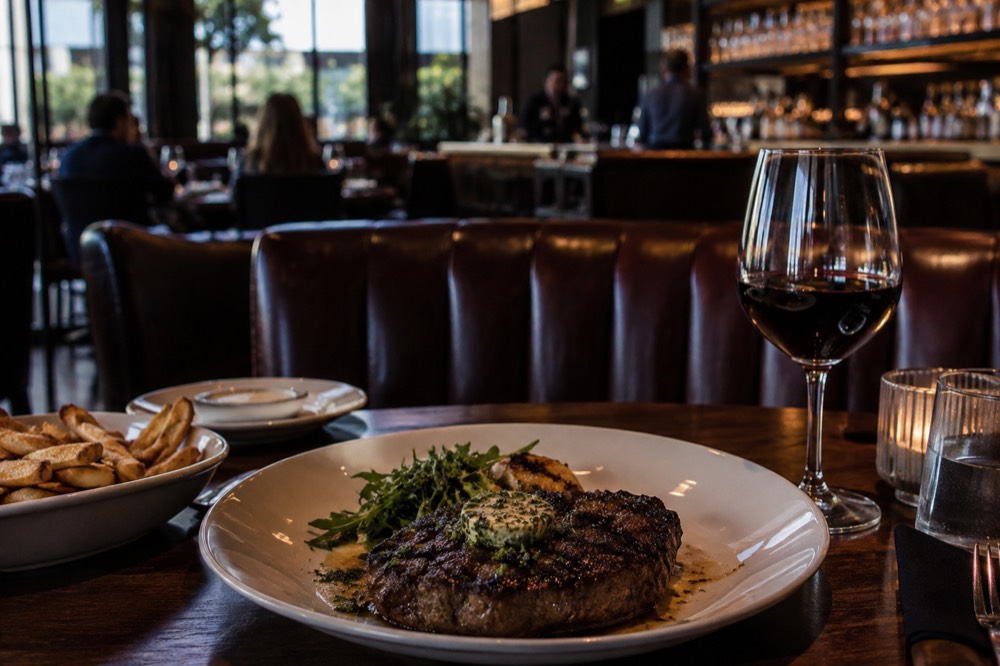 A dimly lit steakhouse dining room with leather banquettes and a bar lined with glassware