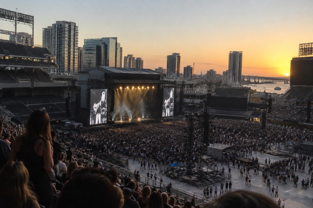 An outdoor stadium in San Diego at dusk with a concert stage and crowd visible across the field