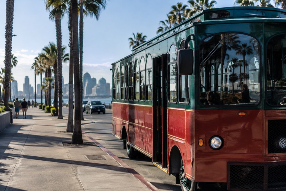 A narrated sightseeing trolley parked on a palm-lined San Diego street near the waterfront