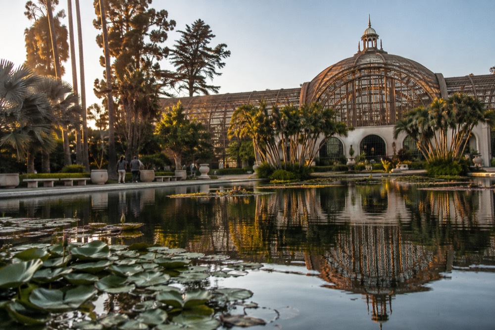 A lattice-domed conservatory building reflected in a still lily pond surrounded by gardens