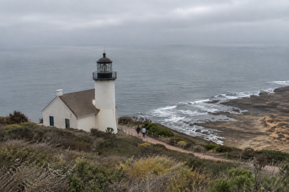 A historic lighthouse on a coastal bluff above tidepools and the open ocean