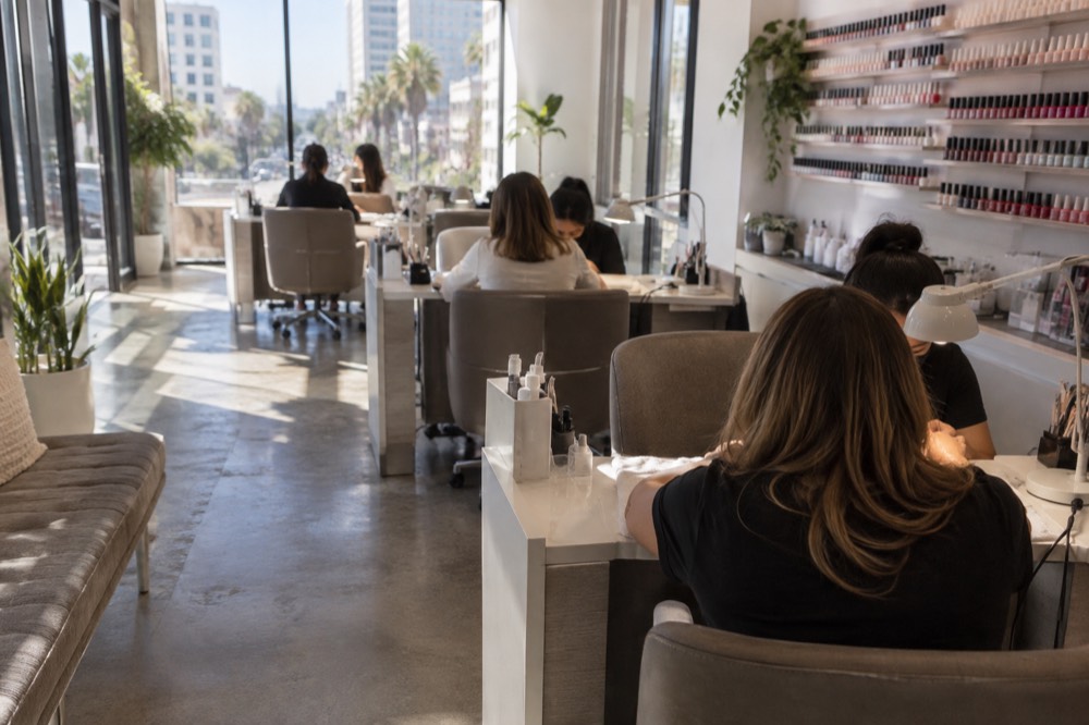 A nail salon interior with rows of manicure tables and polish bottles along the wall