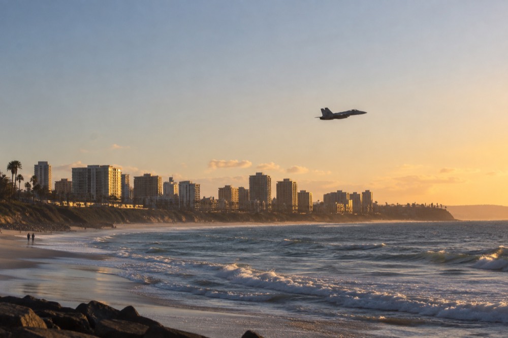 A jet flying over the San Diego coastline with waves breaking below