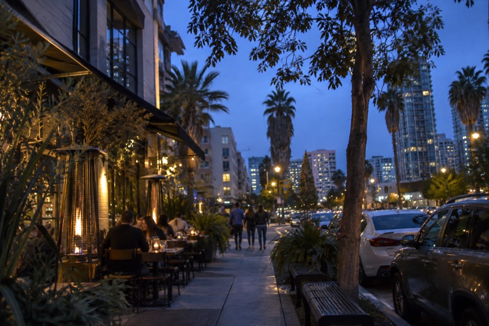 A tree-lined San Diego neighborhood street with small restaurants and sidewalk tables