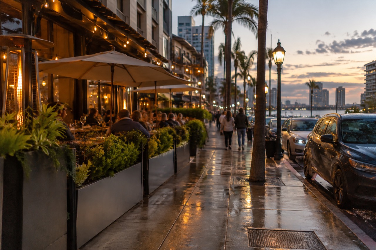 A busy San Diego restaurant street at dusk with neon signs and outdoor tables
