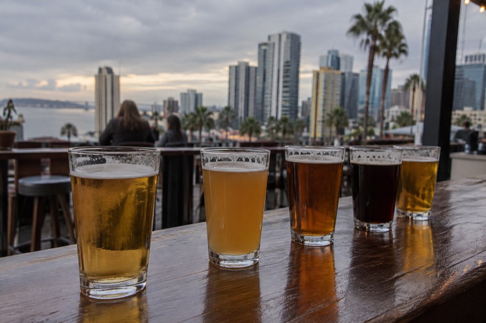 Glasses of craft beer lined up on a wooden bar top in the late afternoon