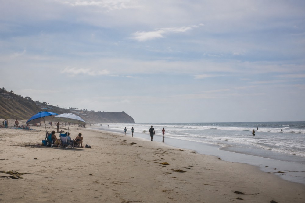 Families with umbrellas on a broad flat beach with soft waves in Del Mar