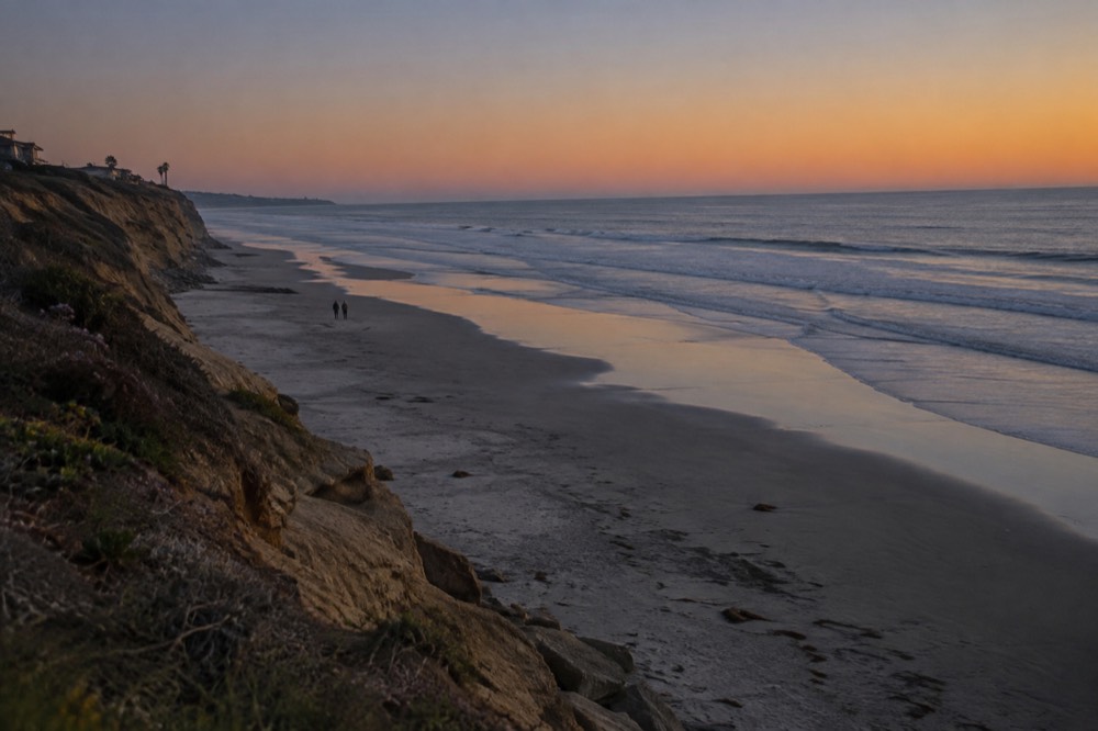 Empty broad beach at golden hour with long shadows toward the water in Del Mar