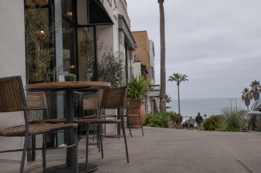 Outdoor café tables on a quiet village sidewalk with storefronts and plants
