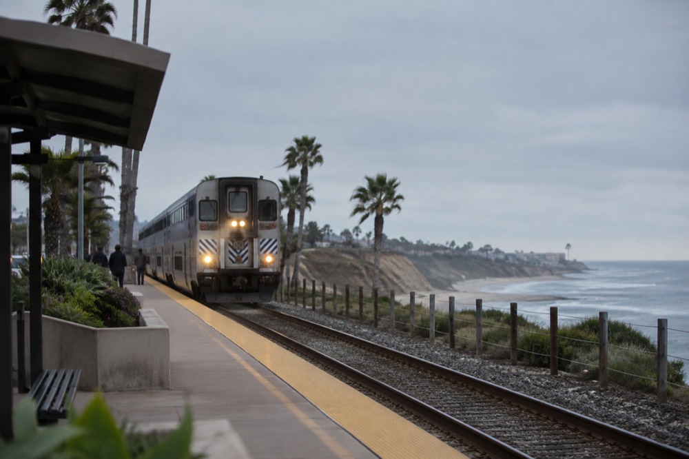 Commuter train arriving at a small coastal station with palm trees