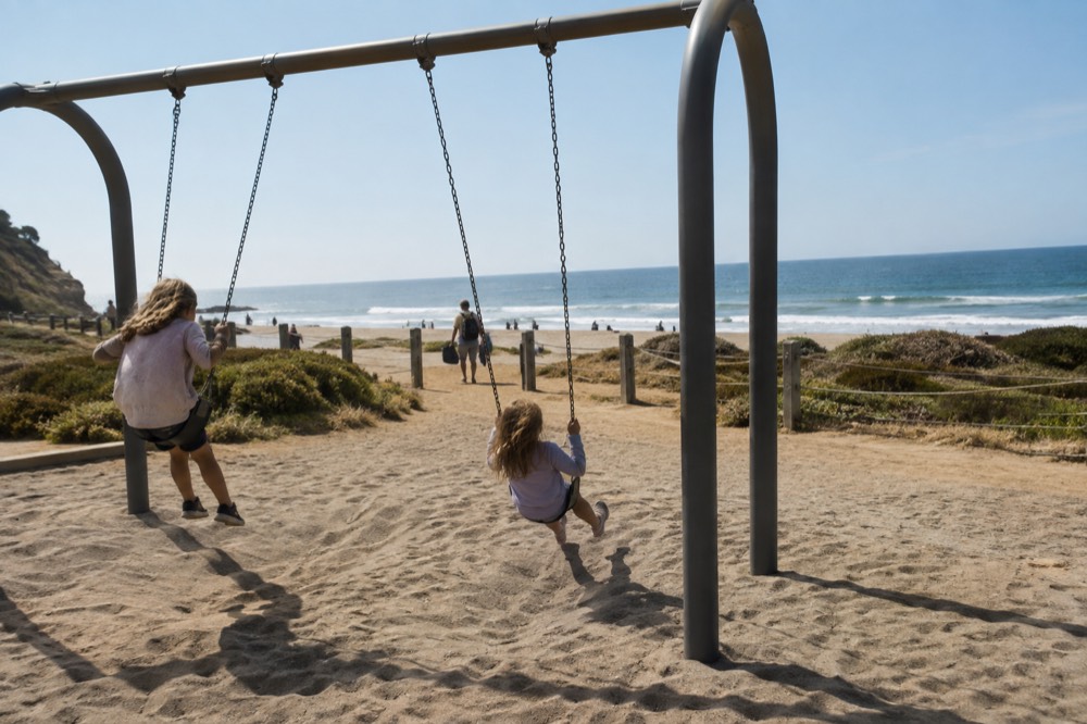 Children playing on a beach playground with swings near the sand