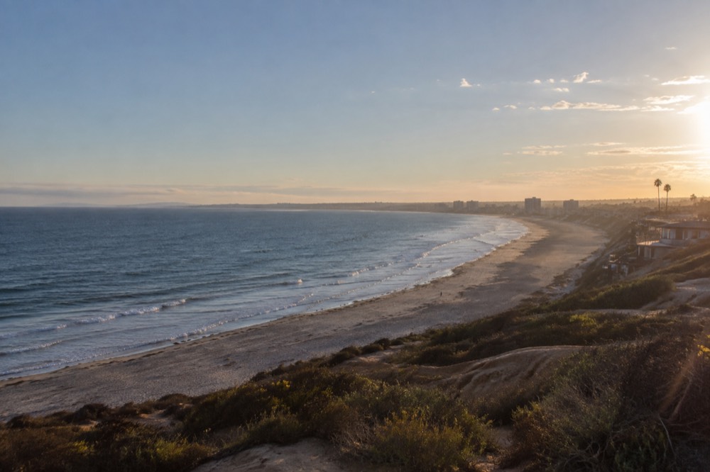 A long curving shoreline seen from above with calm water and distant city buildings