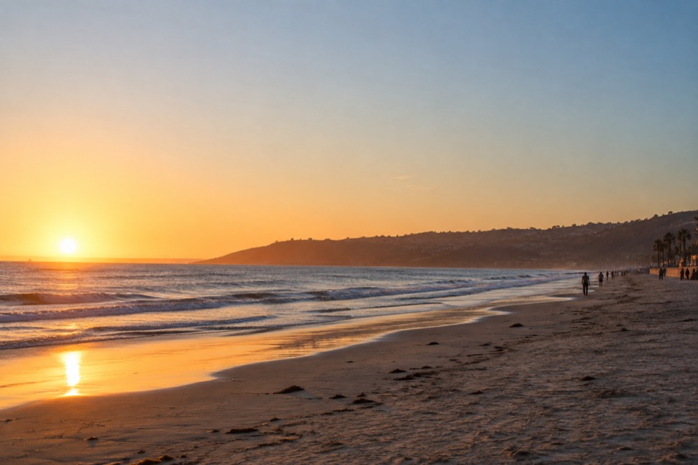 Long flat beach at La Jolla Shores with gentle waves and a boardwalk behind the sand