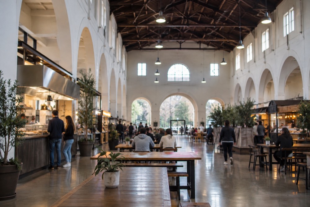 Food stalls and communal tables inside a bright market hall