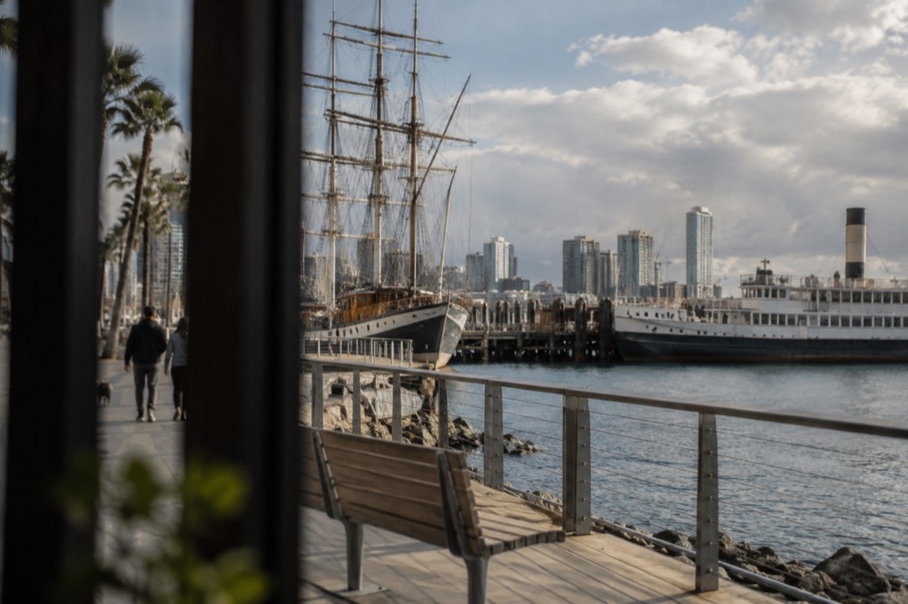 Historic tall ship and steam ferry moored at a wooden pier along a bayfront promenade