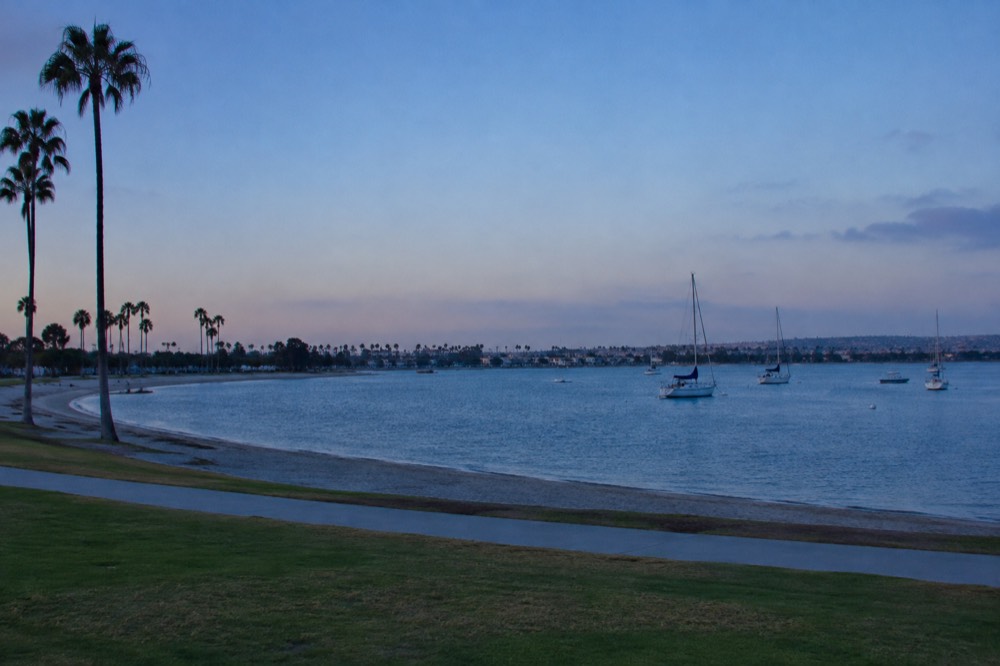 A wide view of blue bay water with sailboats and a clear afternoon sky above the shoreline