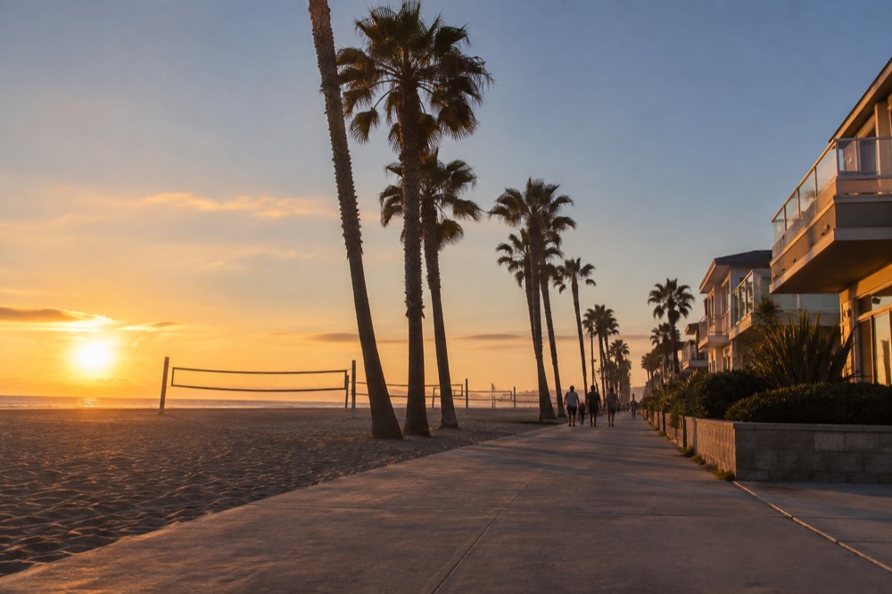 A view down a beach boardwalk with palm trees and beach volleyball courts beside the sand