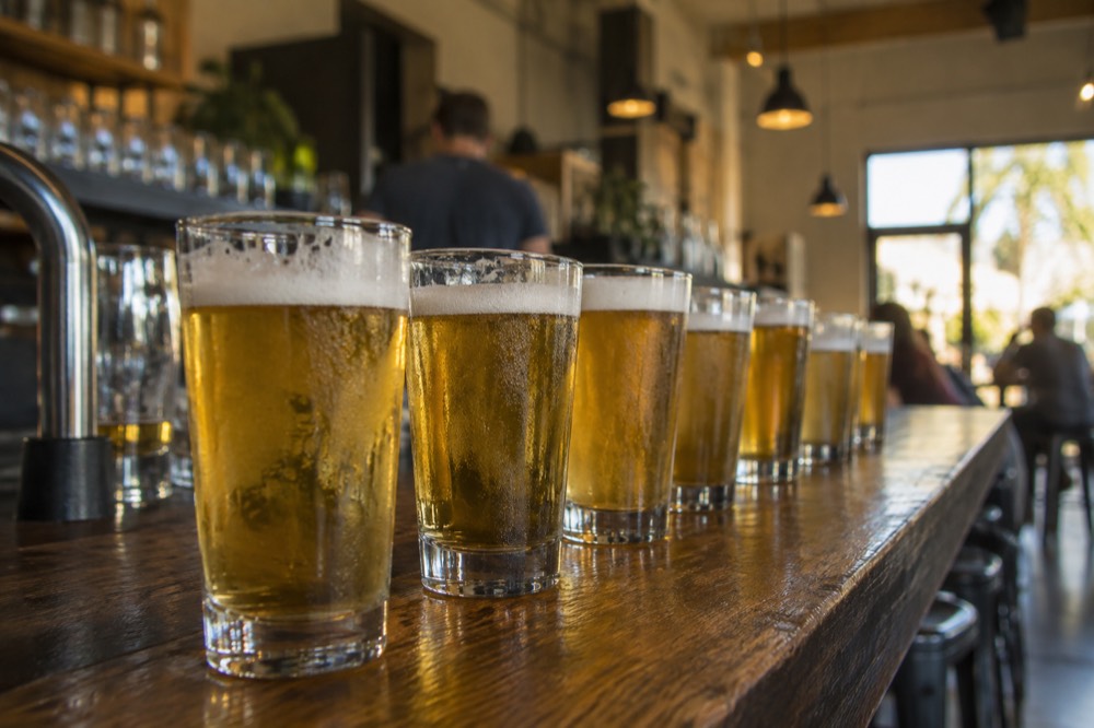 Pints of pale beer lined up on a wooden bar top in a small taproom