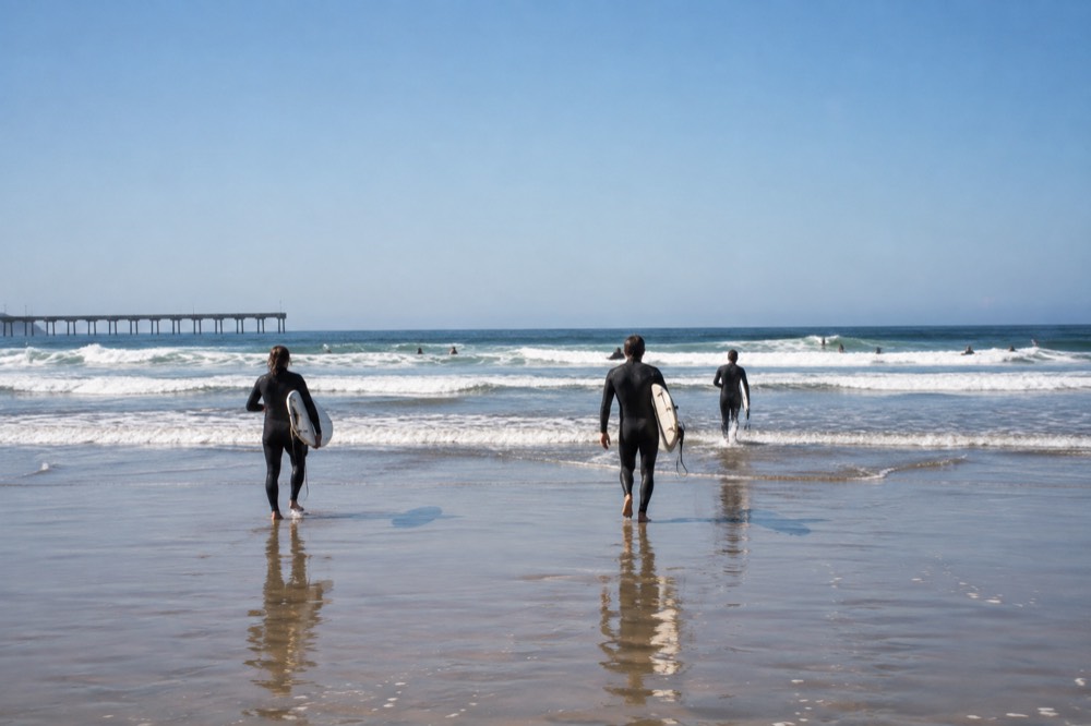 Surfers in wetsuits walking across wet sand toward small waves at Ocean Beach