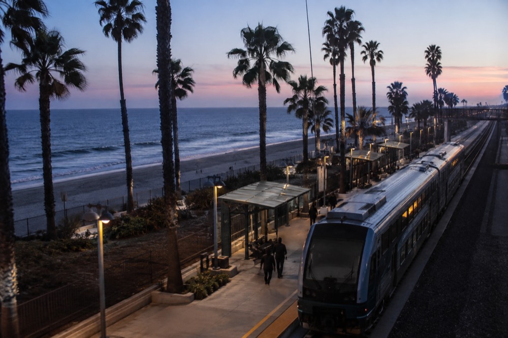 A transit station platform with a modern train and palm trees under a clear sky