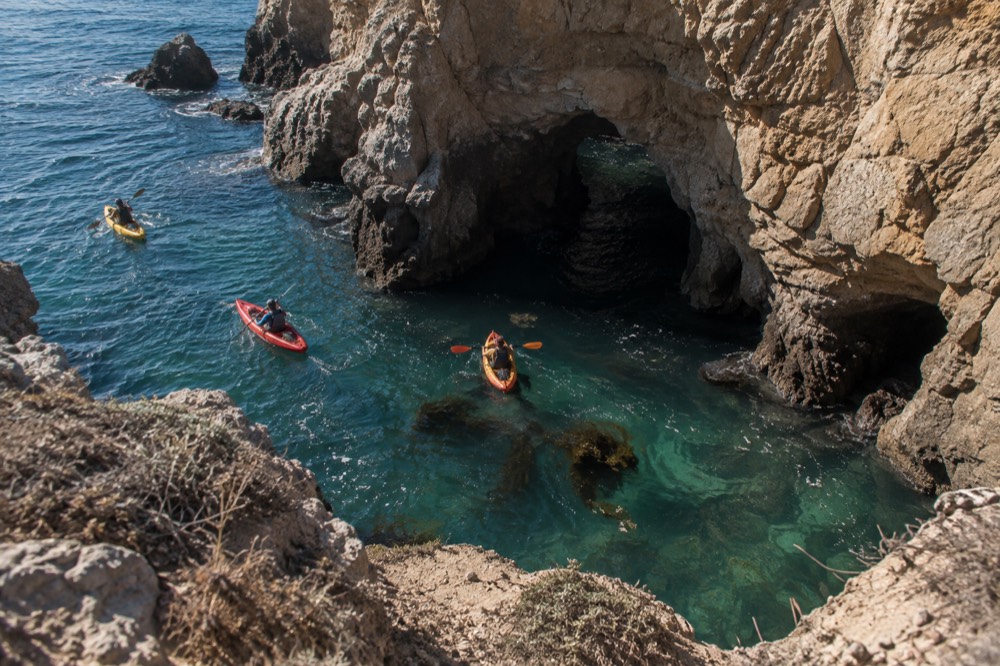 Turquoise water at a rocky cove with kayakers paddling near sea caves