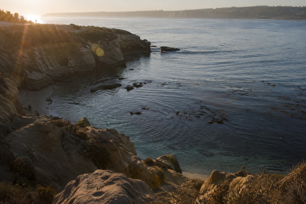 Sandstone cliffs above a calm blue cove with kelp beds visible in clear water