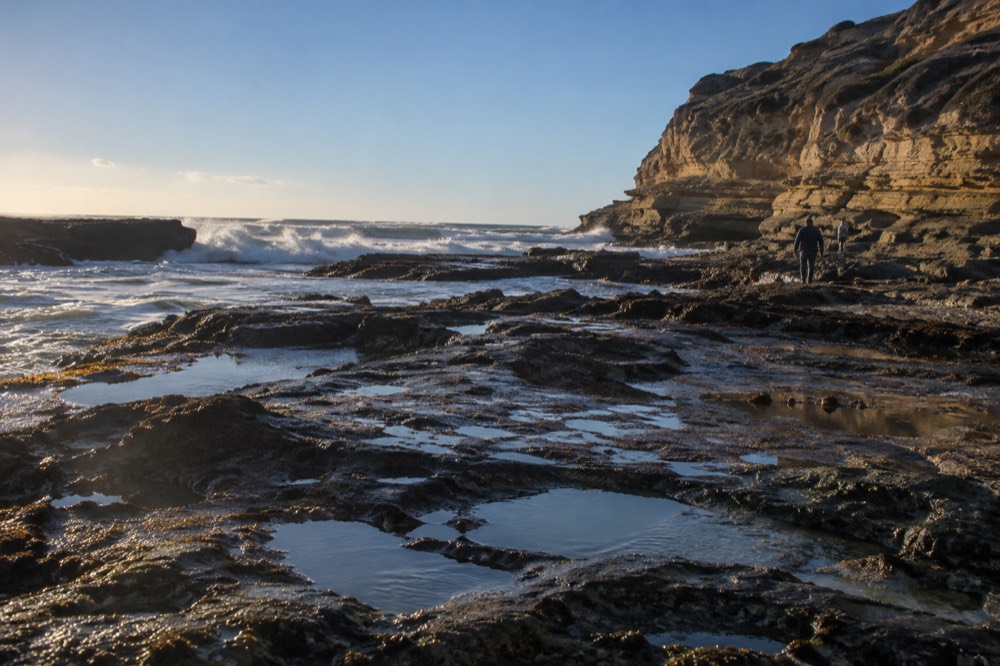 Rocky tide pools at the base of the Point Loma headland with waves breaking beyond