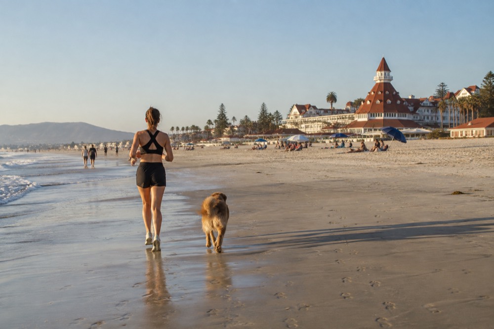 Long stretch of sand with scattered umbrellas and the Hotel del Coronado's red roofs behind