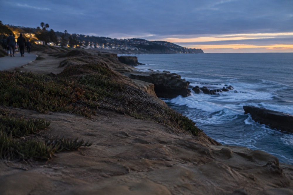 Bluff-top walking path above ocean cliffs with waves breaking below