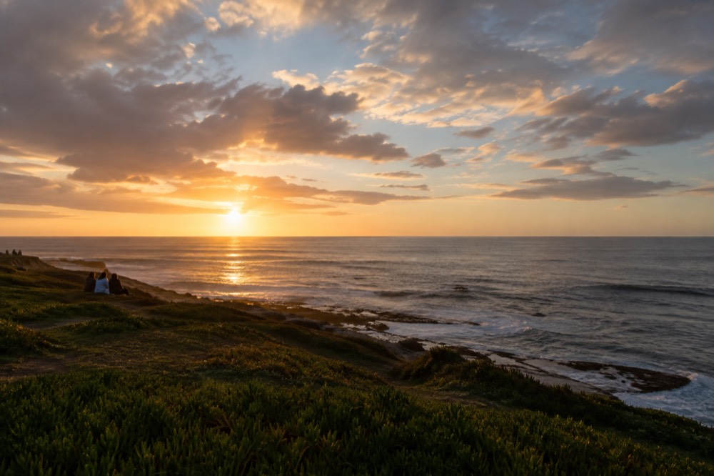 Sunset over the ocean seen from a grassy cliff park above the water