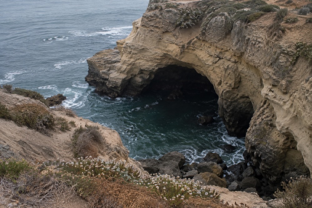 Golden sandstone cliff face with a wide sea cave arch opening onto blue-green ocean water