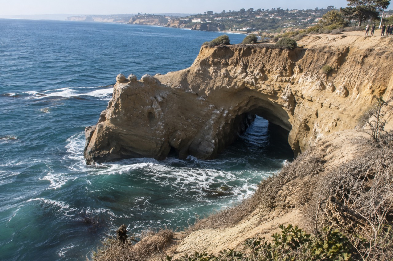 Sandstone cliffs and turquoise water along the La Jolla coastline with a sea cave arch at the base