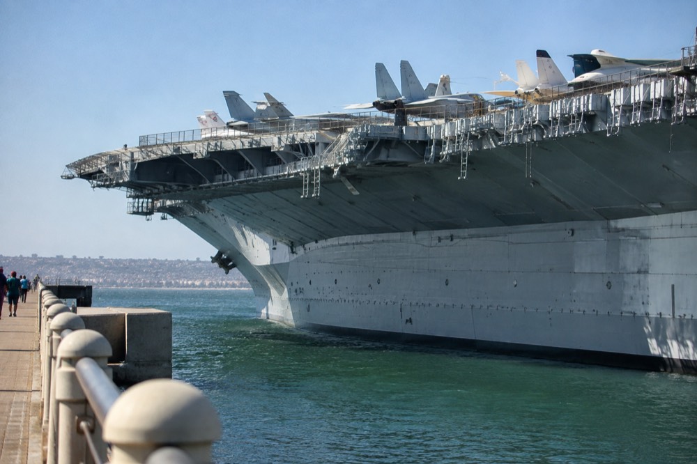 Aircraft carrier flight deck with restored fighter jets parked along the edge