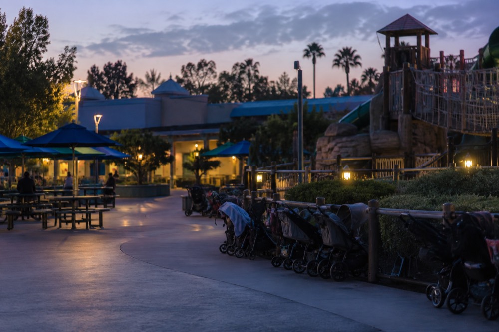 Shaded picnic tables and a stroller parking row beside a themed play structure
